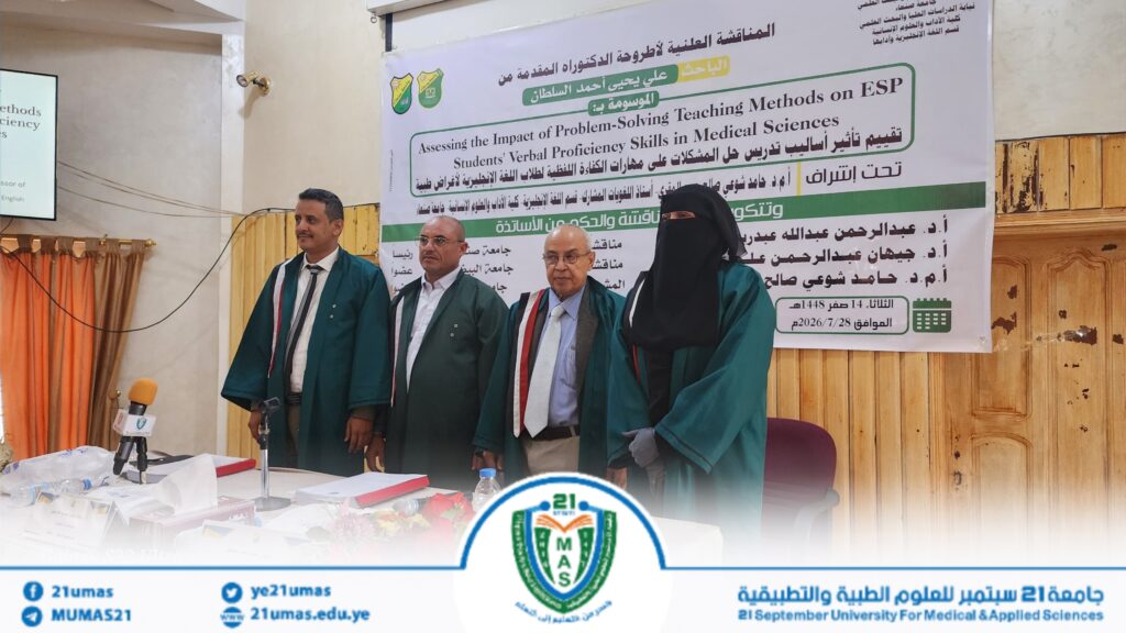 1004053936 - جامعة 21 سبتمبر Four people in green graduation gowns stand on a stage in front of a large banner at a university ceremony.