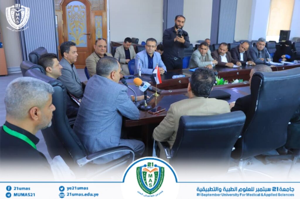 Group of men in a formal meeting around a large conference table, microphones and small flags on the table, a photographer in the background capturing the moment.