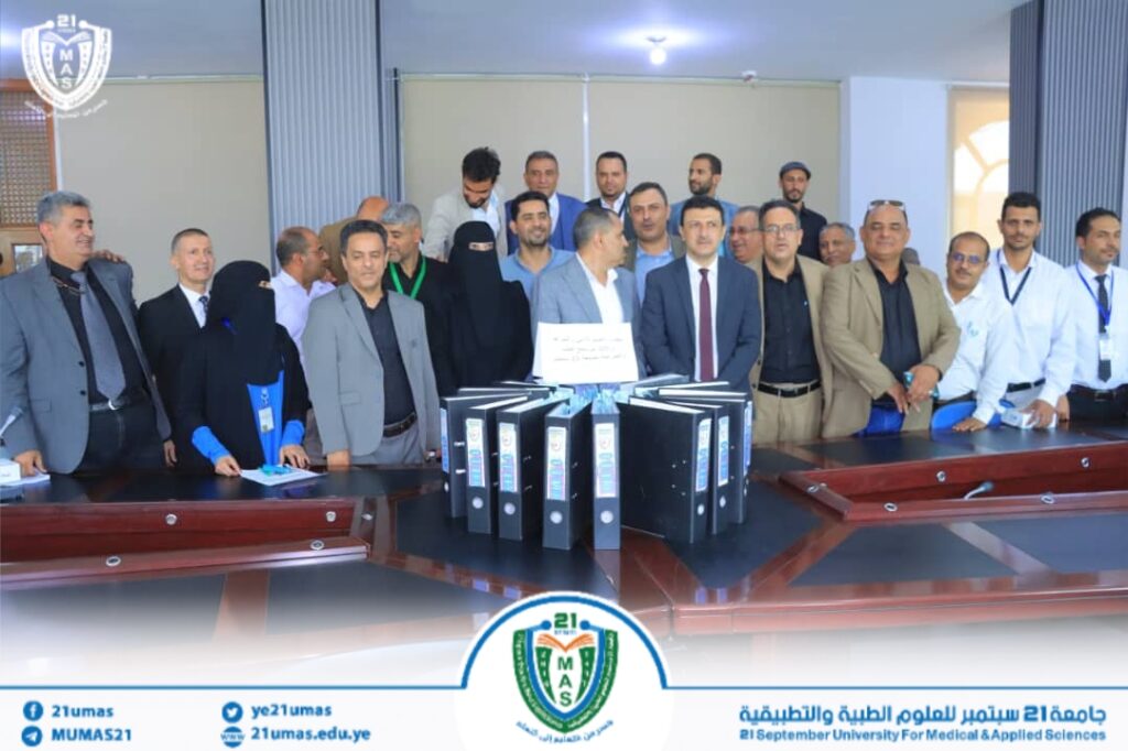 Group of university faculty and staff posing behind a conference table with multiple black binders in front of them. The event appears formal and celebratory at the university setting.