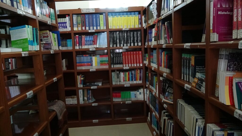 Wooden library shelves filled with textbooks and reference books in a corner study area.