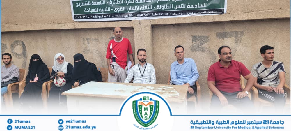 Group of men and women seated on plastic chairs against a wall outdoors, with an Arabic banner fluttering above the scene.
