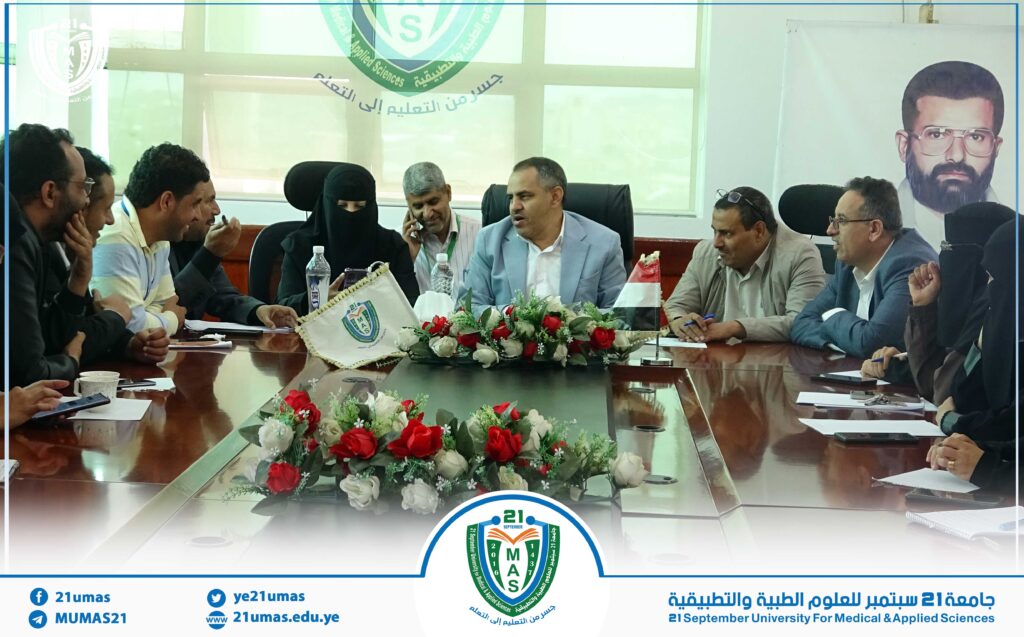 Group of professionals around a conference table in a formal meeting, with a university banner and floral centerpiece, representing 21 September University for Medical & Applied Sciences (MUMAS).