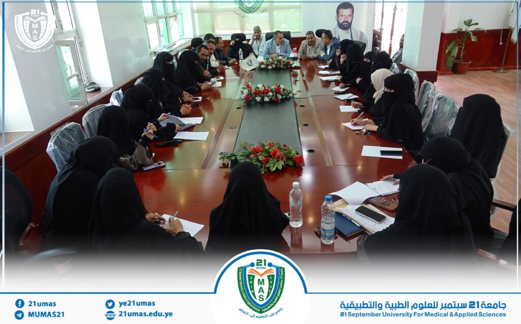 Group of men and women in a formal meeting around a long conference table at a university, with flowers in the center.