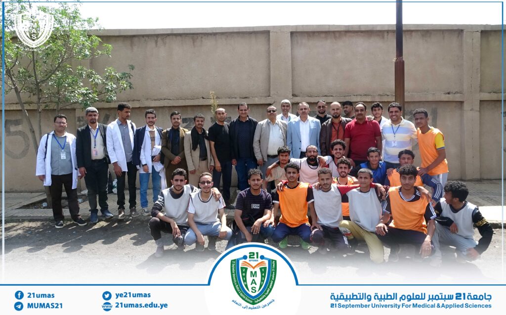 Group of students and staff posing outside a campus wall with the university logo at the bottom center.