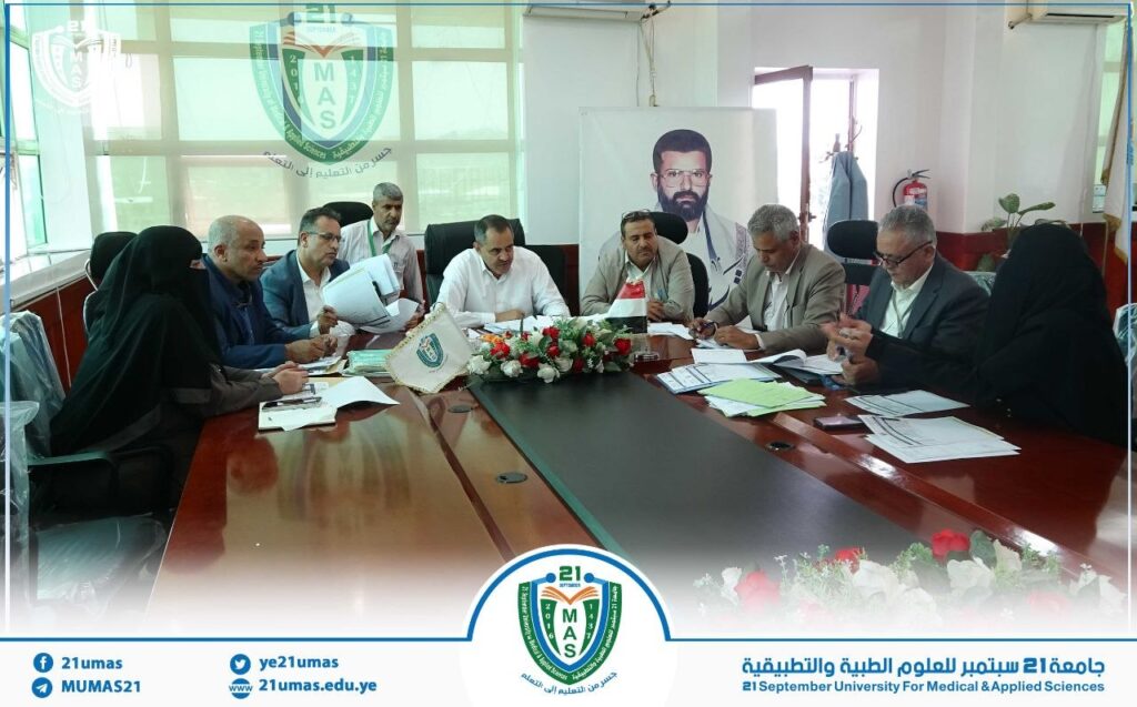 Group of professionals around a conference table reviewing documents, with the university crest visible on the windows behind them.