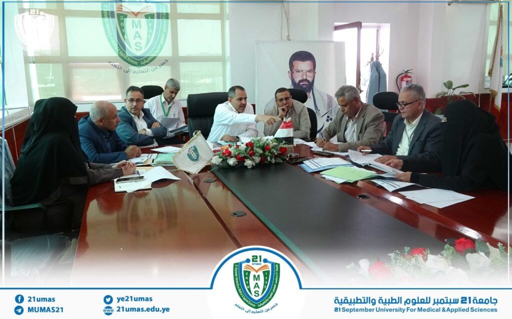 Group of professionals seated around a long conference table, reviewing documents at the 21 September University for Medical & Applied Sciences meeting.