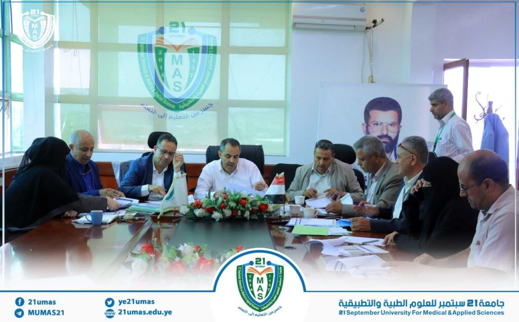 Group of professionals around a conference table reviewing documents, with the university emblem and banners visible in the background.