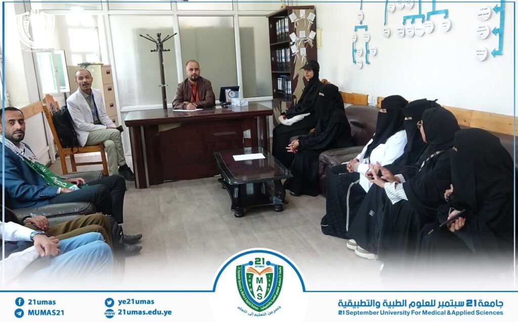 Office meeting: man at desk addresses a group of men and women in traditional dress.