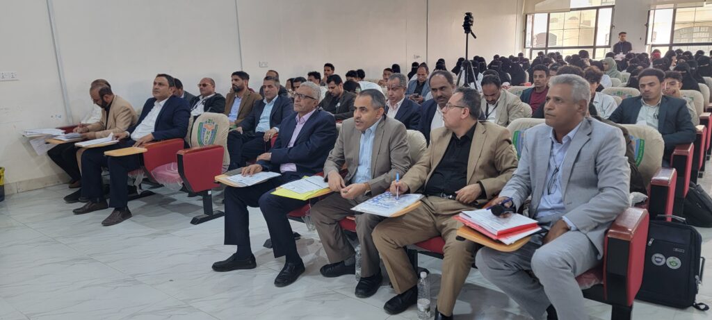 Audience seated in a bright conference room, many in suits, taking notes during a seminar.