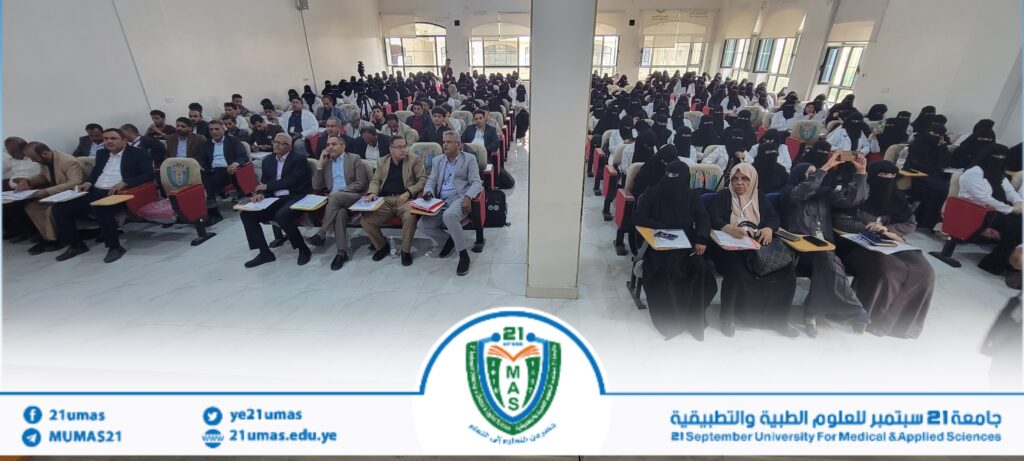 Large conference hall filled with attendees, men in suits and women in hijab, seated and taking notes at a university event.