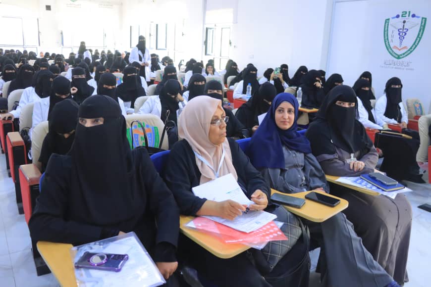 Group of women in a classroom/seminar hall, most wearing black niqabs, seated with notebooks in front row.