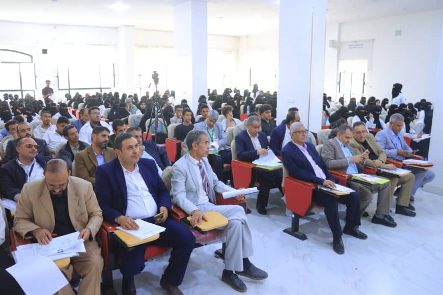 Large audience seated in a conference hall, front row men in suits with folders and papers.