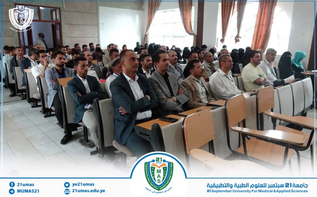 Audience seated in a lecture hall listening to a presentation at a university event. Logo and banners for 21 September University of Medical & Applied Sciences visible at the front border.