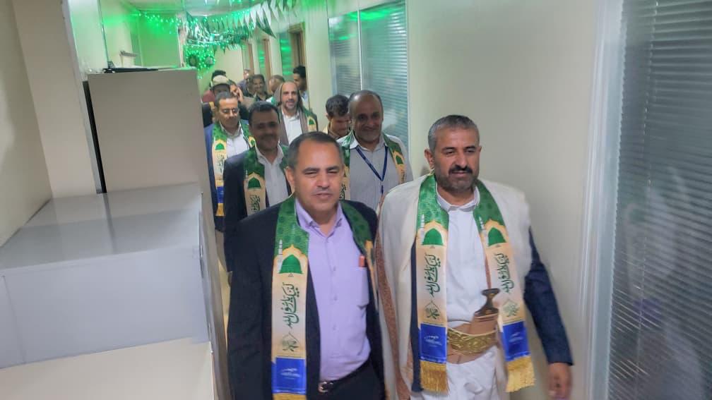 Group of men in a hallway wearing green and gold ceremonial sashes, walking toward the camera.