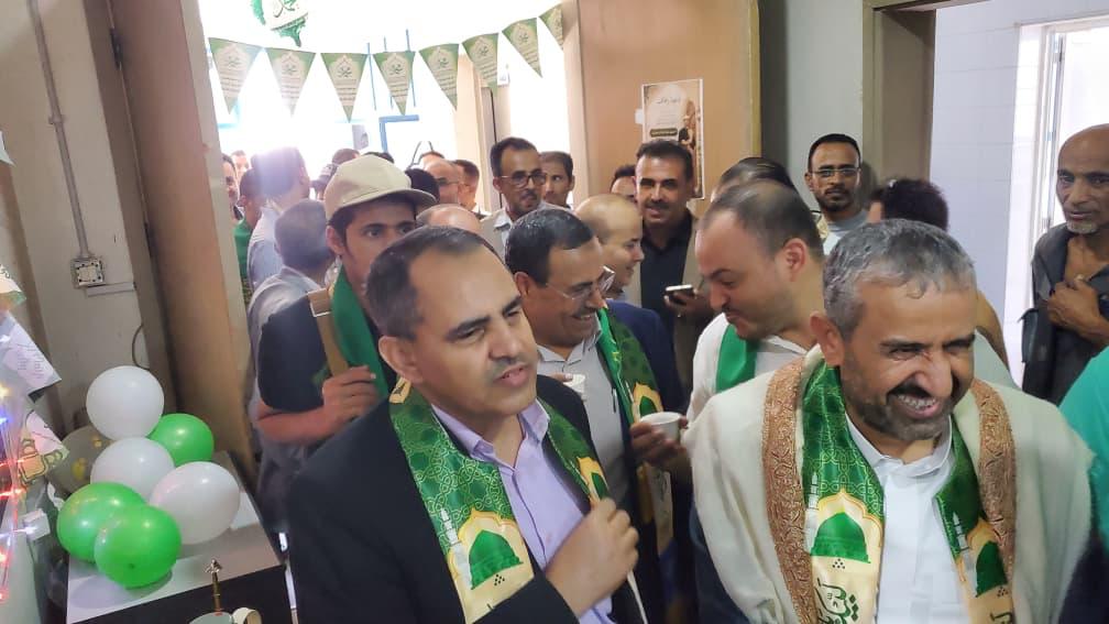 Group of men wearing green scarves at a festive indoor gathering, with green and white balloons in the corner.
