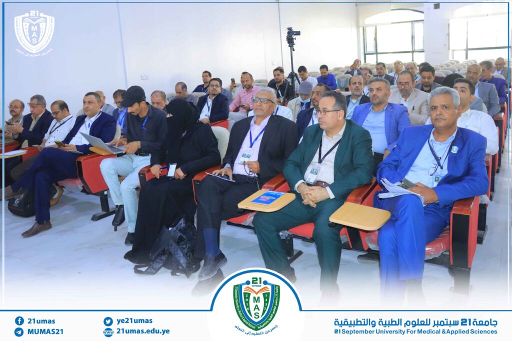 Audience of professionals seated in a bright lecture hall attending a conference at 21 September University for Medical & Applied Sciences; a camera on a tripod is set up at the back.