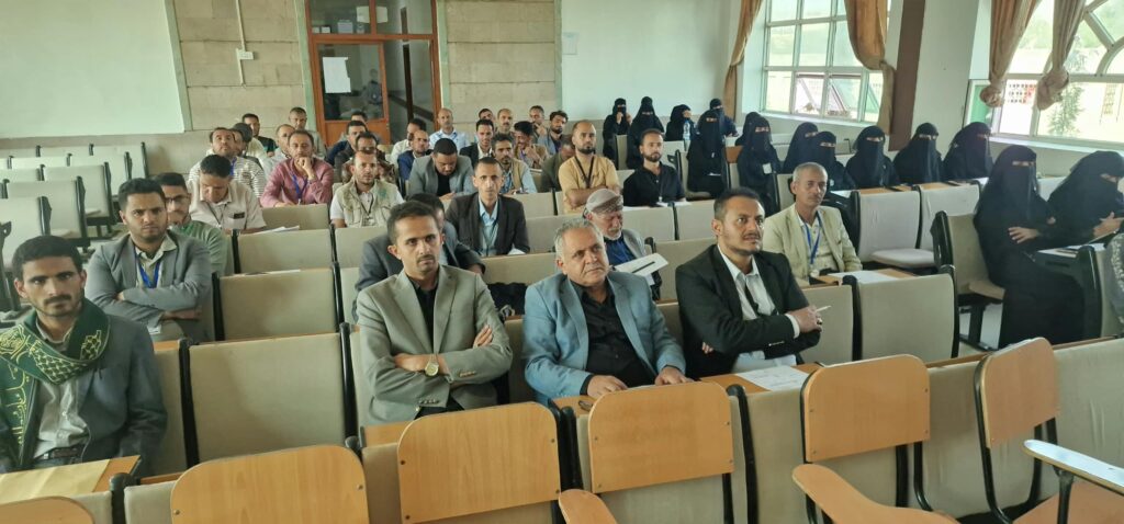 1001242626 - جامعة 21 سبتمبر Audience seated in a classroom lecture hall; men in front rows, women in black niqab in back row(s).