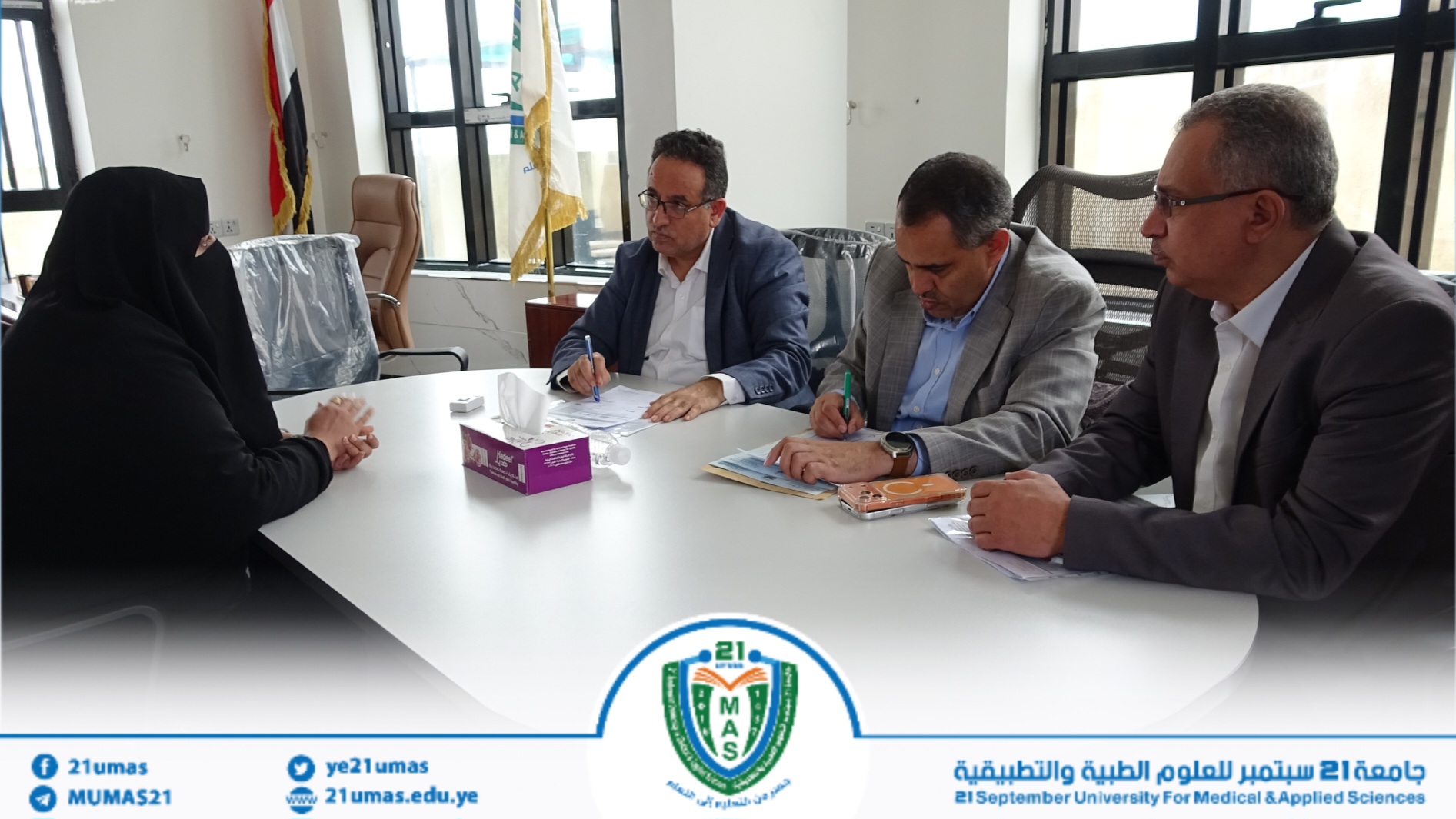 Group of professionals seated around a table signing documents during a formal meeting in a university office.