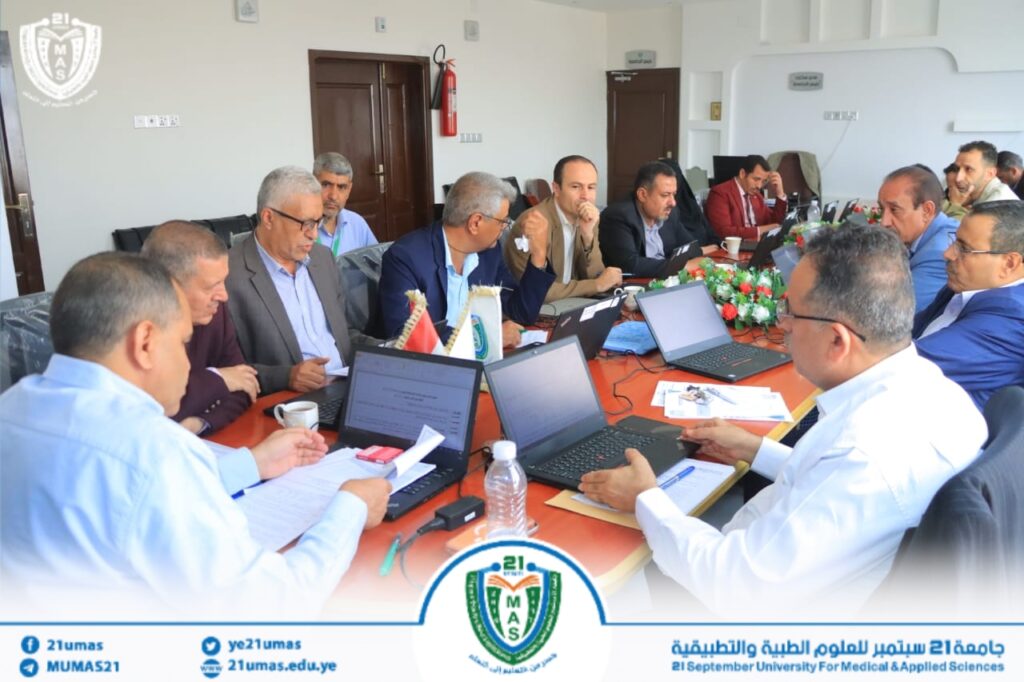 University meeting: faculty and staff sit around a long conference table with laptops and documents in view.