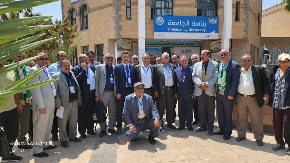 Group of men in suits posing for a photo in front of Presidency University building on a sunny day.