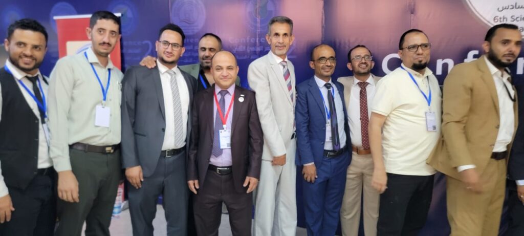 Group of men in suits and badges posing for a photo at a conference with a purple backdrop behind them.