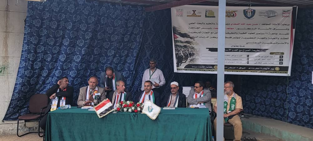 Panel of men seated behind a long table on a stage, with banners and floral centerpiece in front at a formal conference.