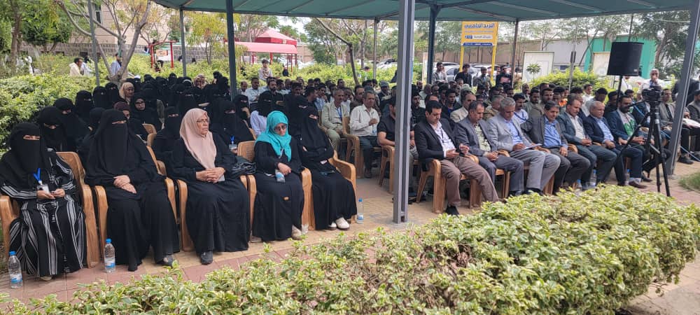 Outdoor ceremony or meeting under a canopy with rows of attendees, many women in black abayas and men in suits in the front rows.