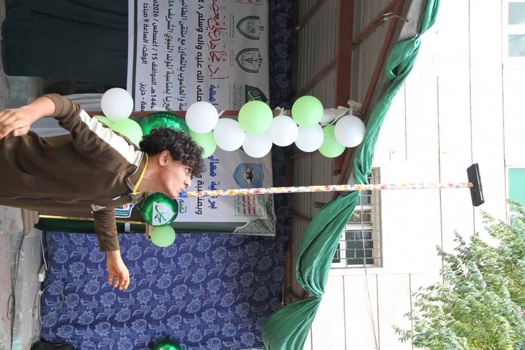 Young man in a brown outfit on a decorated stage with green and white balloons.