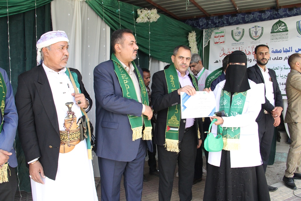 Dignitaries in green sashes present a certificate to a woman in a niqab at a ceremony under a tent.