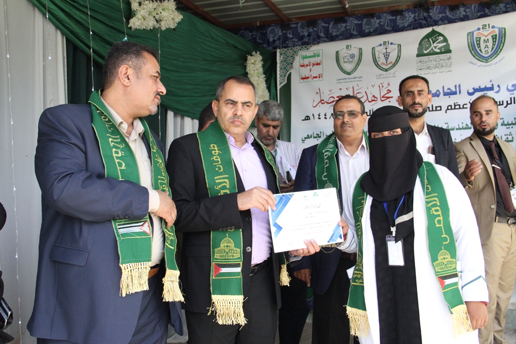 Group of professionals at an award ceremony; a man in a suit hands a certificate to a woman wearing a hijab and lanyard, all wearing green sashes with gold detailing.