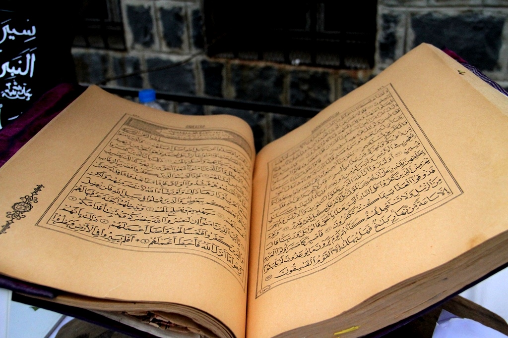 Open Qur'an on a stand, pages showing dense Arabic calligraphy and borders.