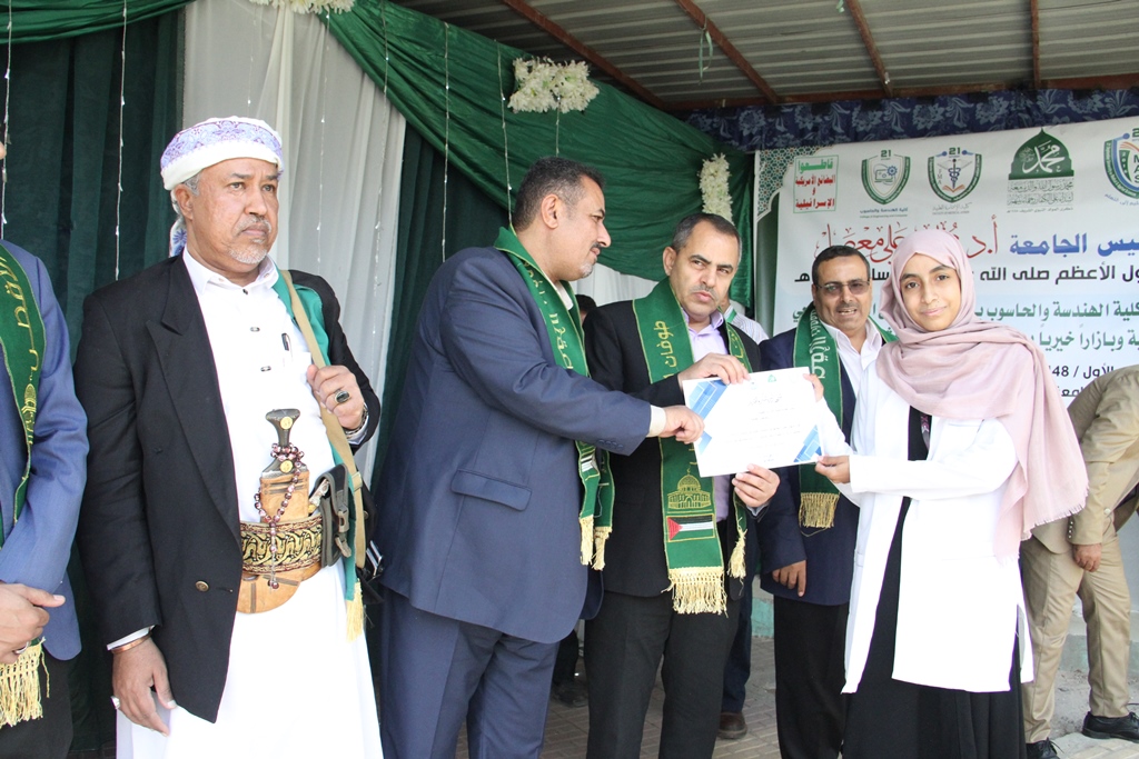 Group of men in suits with green sashes presenting a certificate to a young woman in a hijab at an outdoor ceremony.