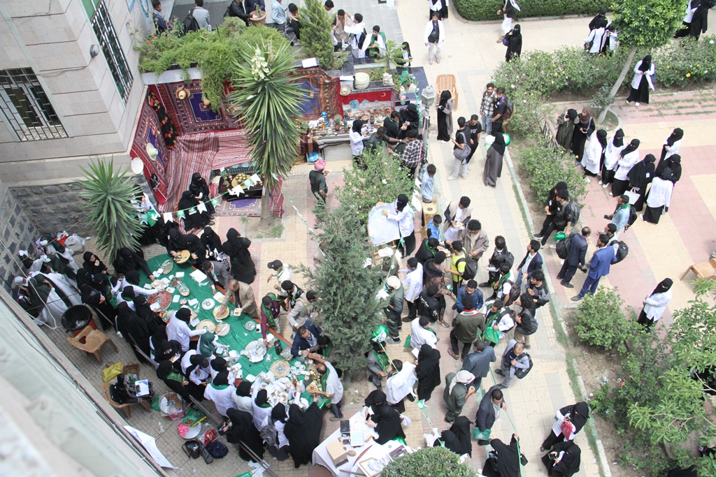 Overhead view of a busy outdoor market or fair with stalls, tables, and crowds of people walking and shopping.