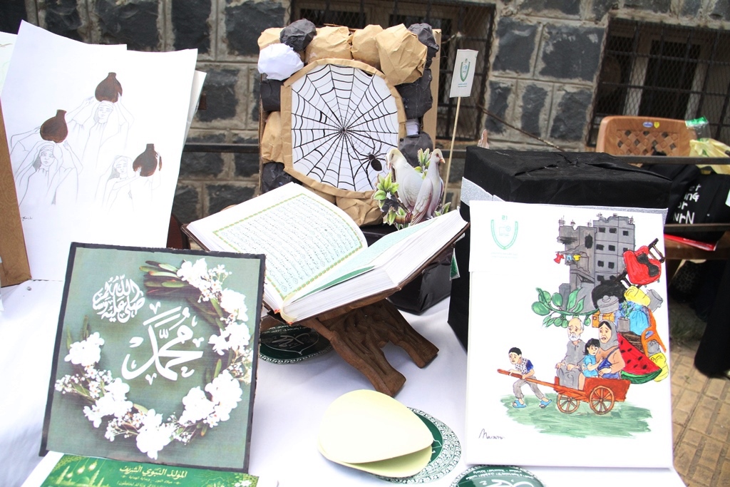 Outdoor display table with Islamic books and art: an open Qur'an on a wooden stand among posters and artwork.