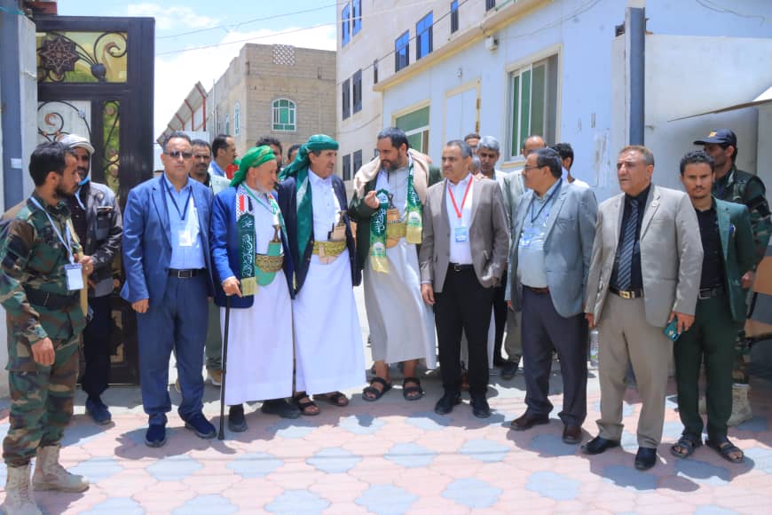 Group of men in traditional dress and suits posing together outdoors on a sunny street.