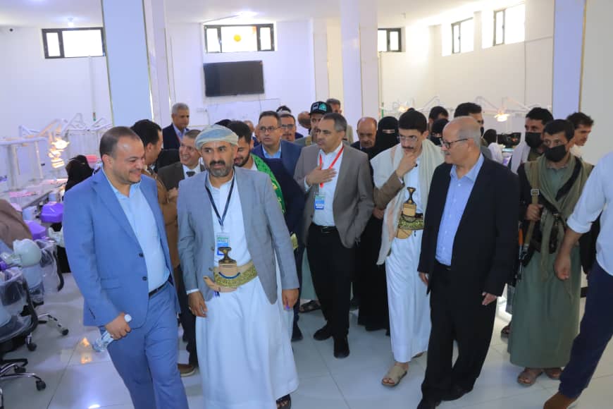 Group of officials on a tour inside a bright medical facility; several men in suits and traditional robes lead the way.