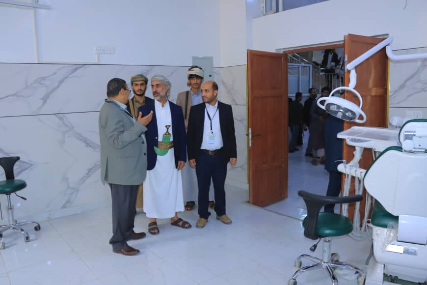 Group of men in a clinic talking, with a dental chair and equipment visible to the right and an open door in the background.