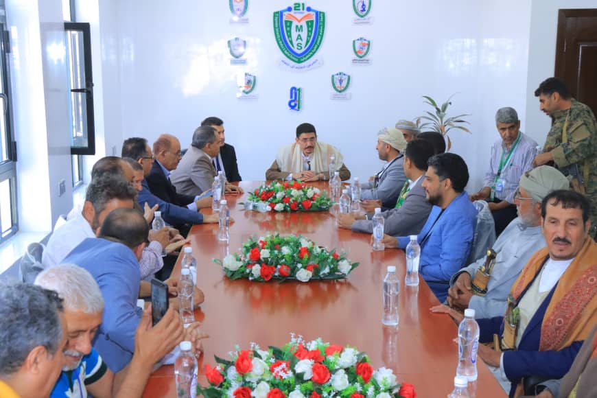 Group of men seated around a long conference table, center man speaking at a formal meeting.
