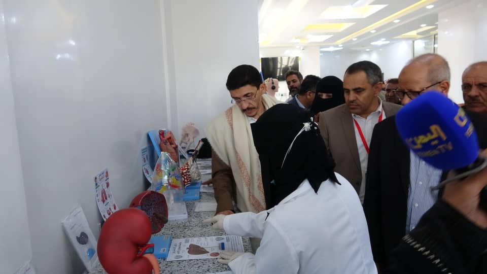 Medical professional in a white coat explains medical devices and brochures laid out on a counter to a group of visitors at a clinic exhibit.