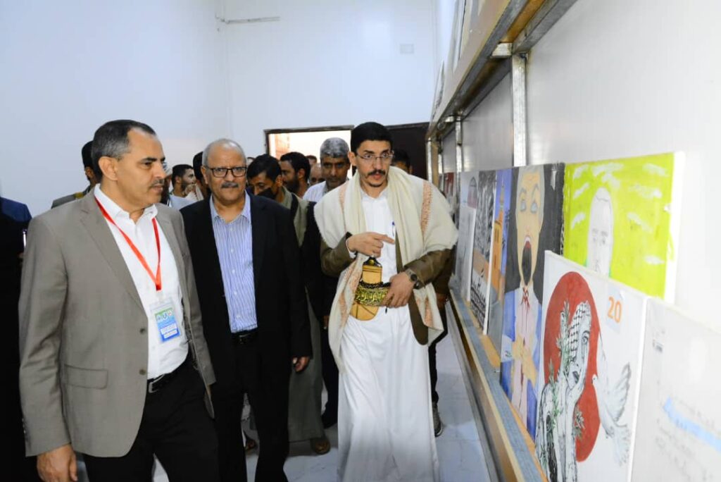 Group of men in suits walking along a wall of colorful posters in a gallery or hallway exhibition.