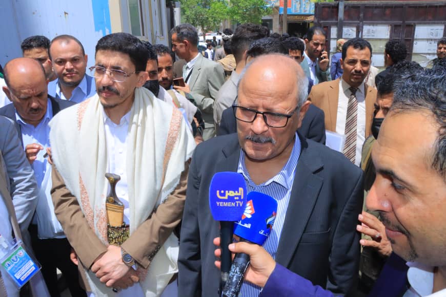 Man in suit being interviewed by Yemen TV reporters outdoors, multiple journalists around him, microphones visible with Yemen TV logos.