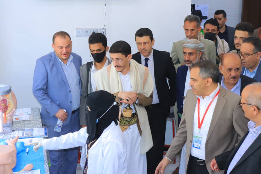 Medical demonstration: a clinician in a hijab explains a procedure to a group of men in business attire gathered around a table with medical supplies.