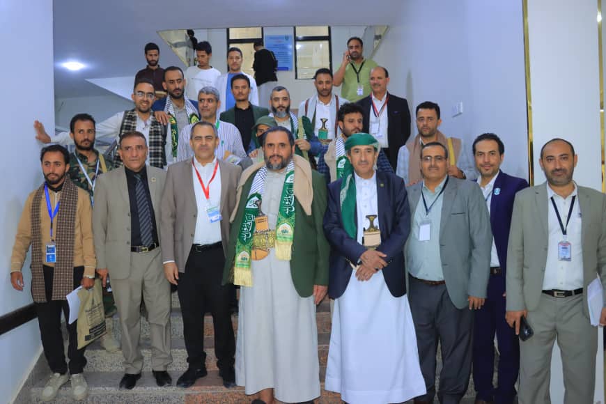 Group of men in suits and traditional dress posing on a stairwell at a conference venue.