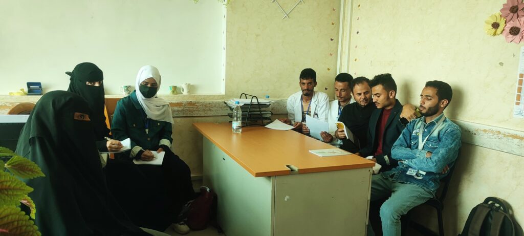 Group of men and women sitting in a clinic or classroom, reviewing documents at a long table.