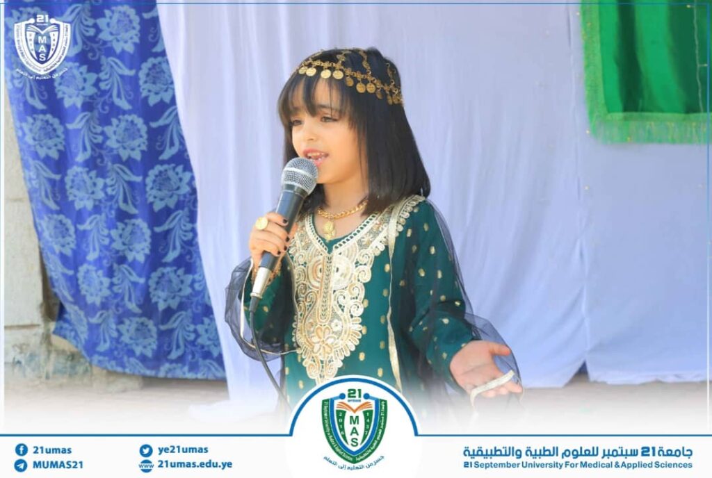 Young girl in a green traditional dress sings into a microphone on a stage at a university event banner.