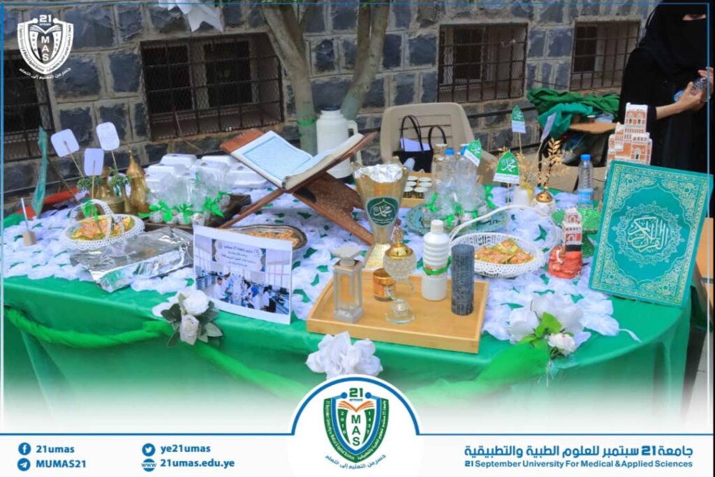 Display table with Islamic items, a Quran on a wooden stand, decorative bottles, and green accents at a university event booth