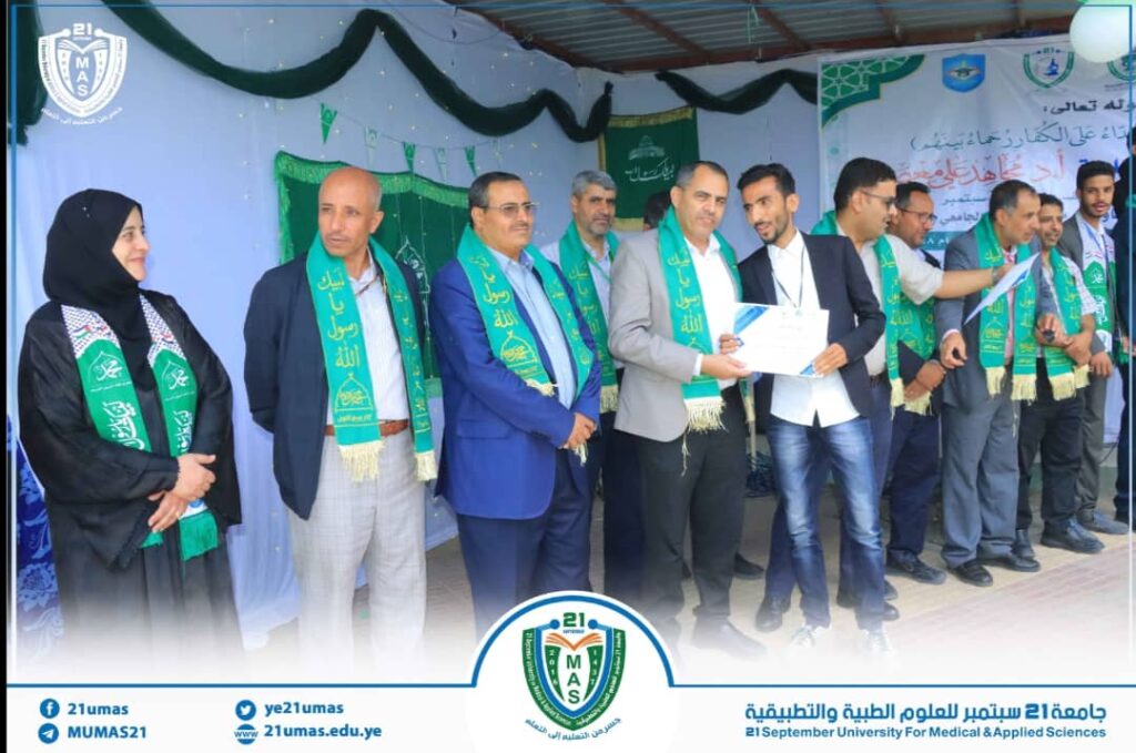 Ceremony on stage with men and a woman wearing green sashes, one person handing a certificate, banners and logos in the background.