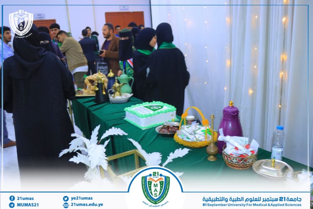 Group of people at a university event around a table with a cake and refreshments, banner and logo visible in the foreground.