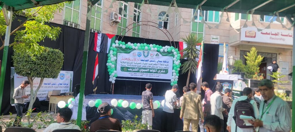 Outdoor ceremony on a stage with green/white balloons and a banner, group of people gathered for an event.