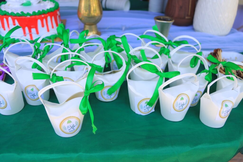 Row of white gift bags tied with green ribbons on a green table at a celebration event.